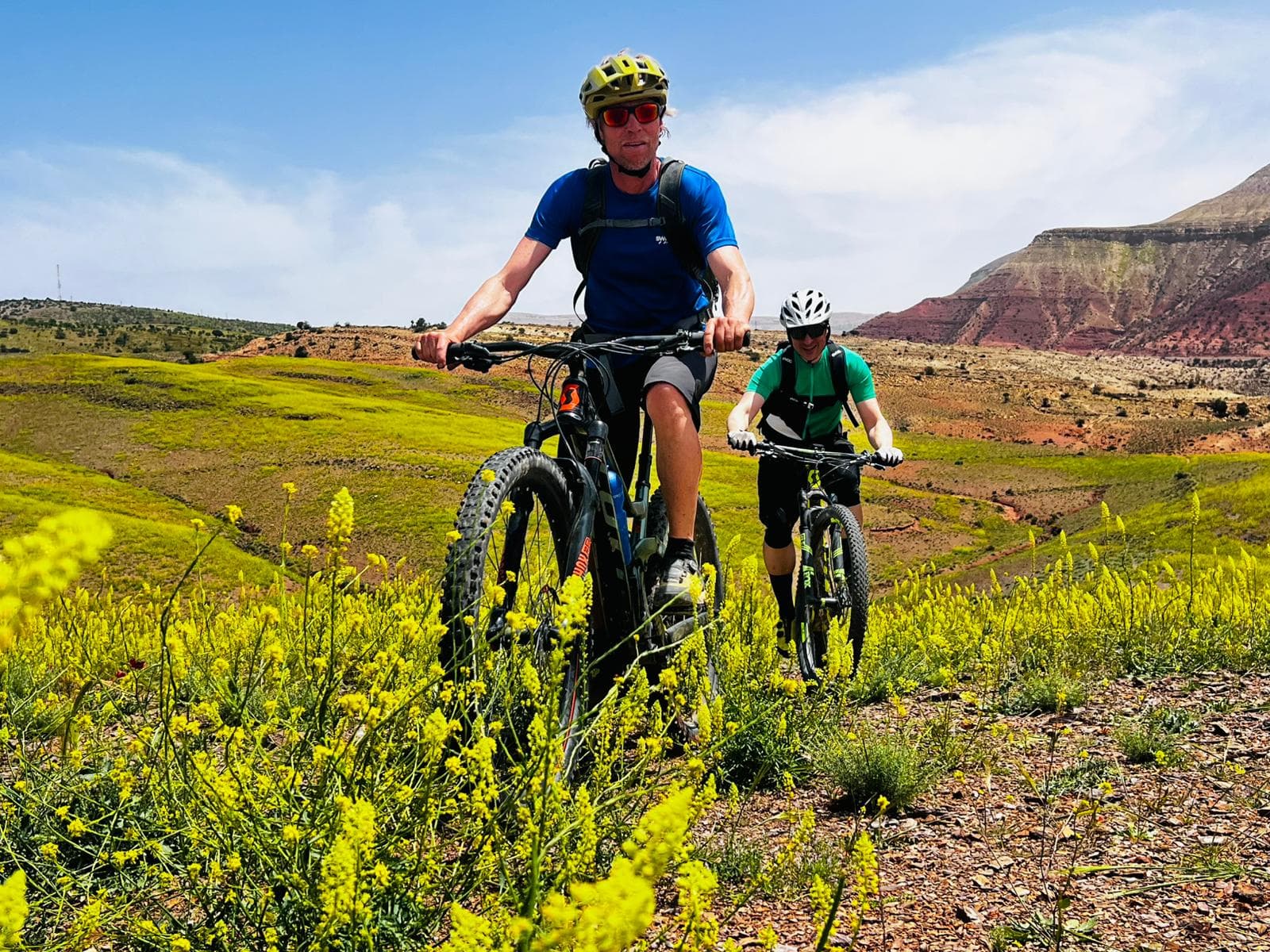 Two riders crossing a green mountain landscape